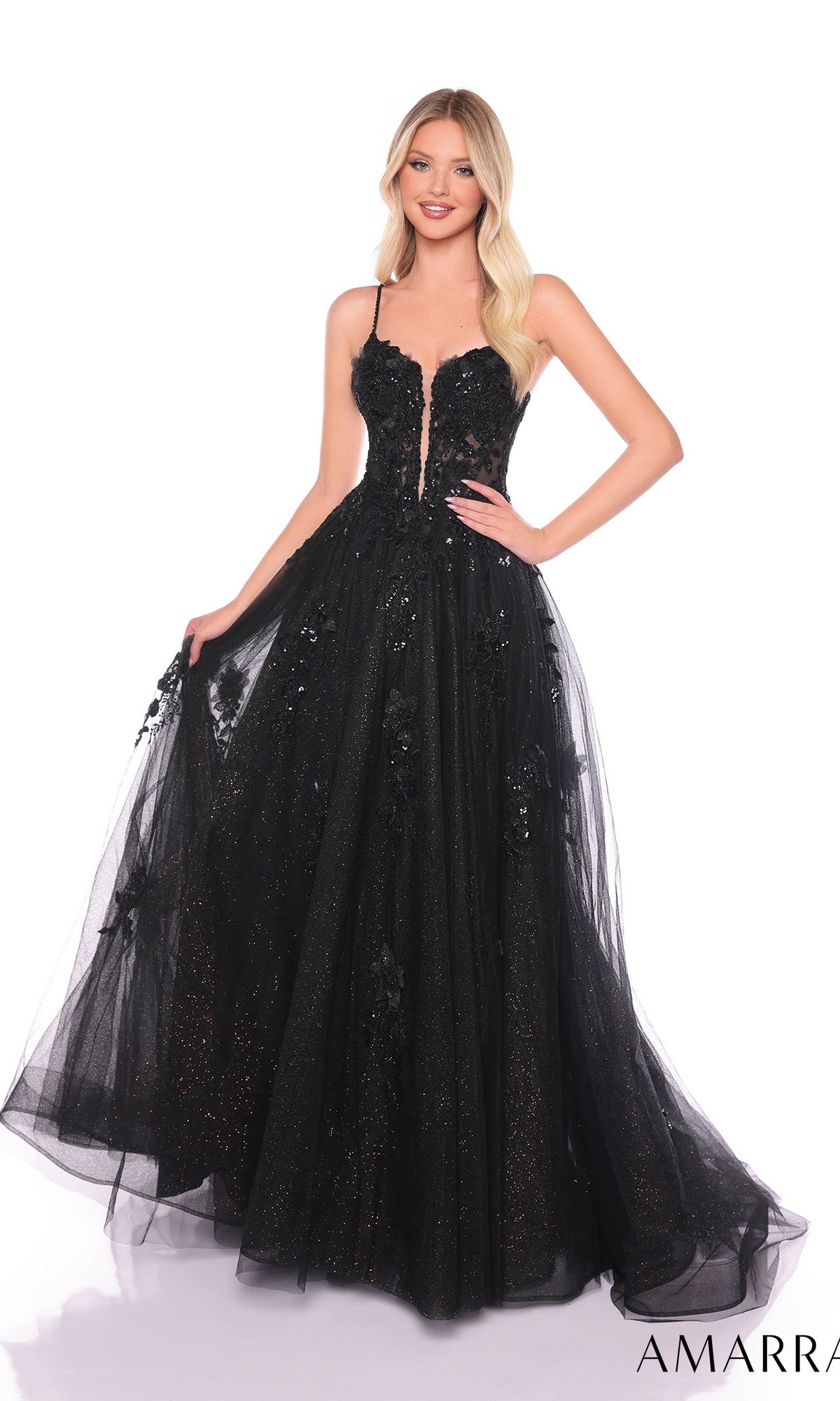 A woman stands against a white background wearing the Amarra 88086, a long formal black ball gown with sleeveless design, floral appliqu‚s, lace embroidery, and glitter details.
